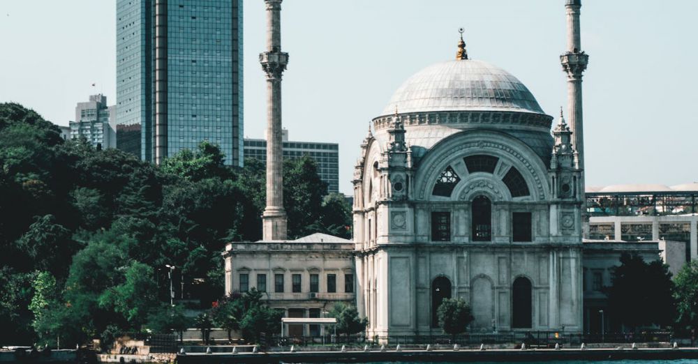 Cultural Tours - Scenic view of a historic mosque and modern skyline by the water, under a clear sky.