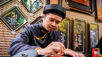 Indigenous Languages - An artist in traditional attire creates beautiful Vietnamese calligraphy indoors.