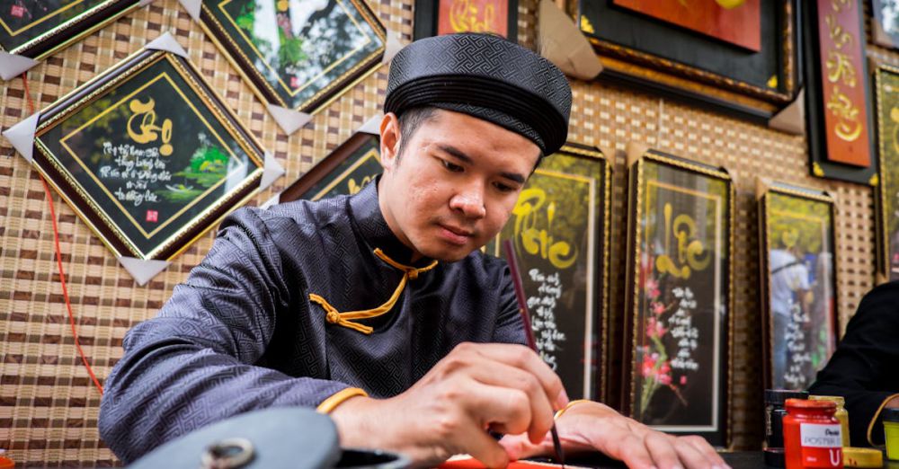 Indigenous Languages - An artist in traditional attire creates beautiful Vietnamese calligraphy indoors.