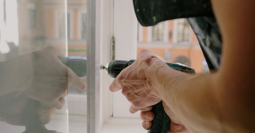 Cordless Drills - Close-up of a handyman's hands using a drill to fix a window inside an apartment.