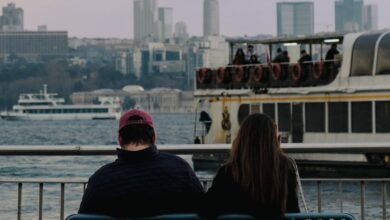 Couple Experiences - Couple seated on a bench, gazing at boats on the Istanbul waterfront with city skyline.