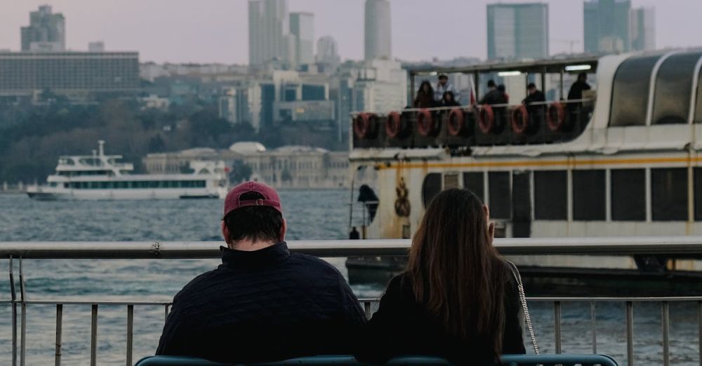 Couple Experiences - Couple seated on a bench, gazing at boats on the Istanbul waterfront with city skyline.