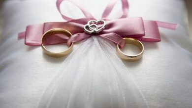 Engagement - Close-up of elegant wedding rings on a silk pillow with a pink ribbon and a heart decoration, symbolizing love.