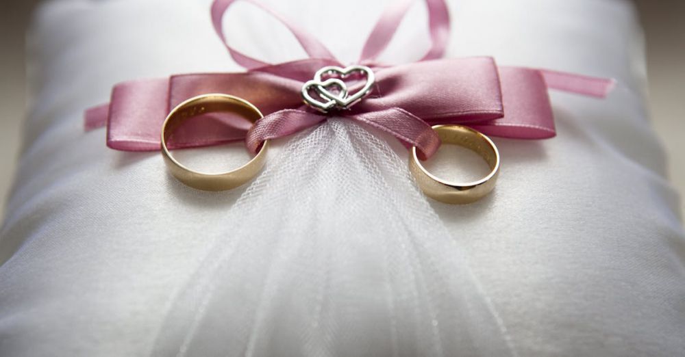 Engagement - Close-up of elegant wedding rings on a silk pillow with a pink ribbon and a heart decoration, symbolizing love.