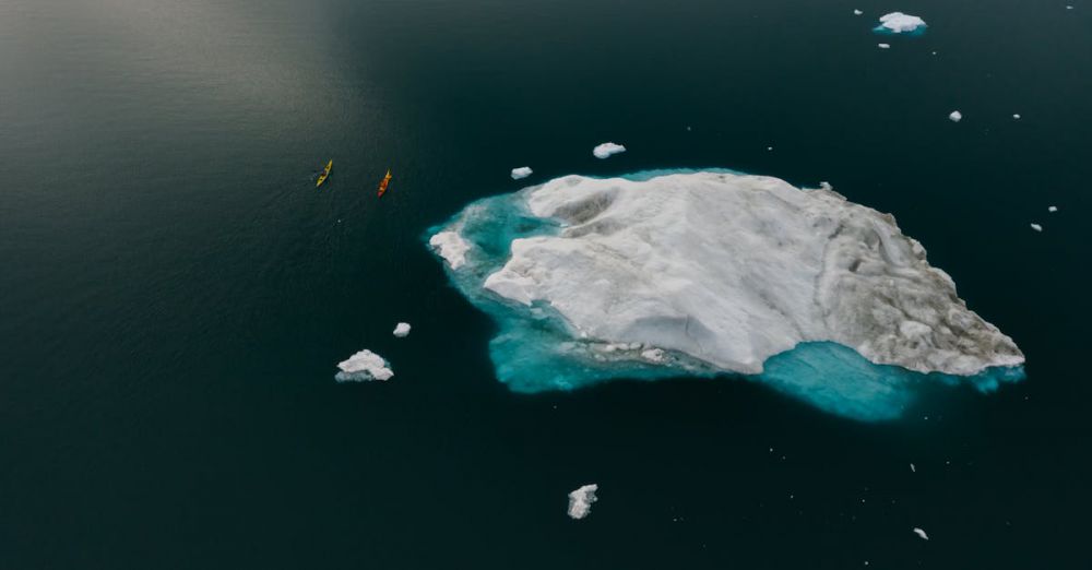 Kayaking Destinations - Drone shot capturing colorful canoes navigating near a large iceberg in cold waters. Winter adventure scene.