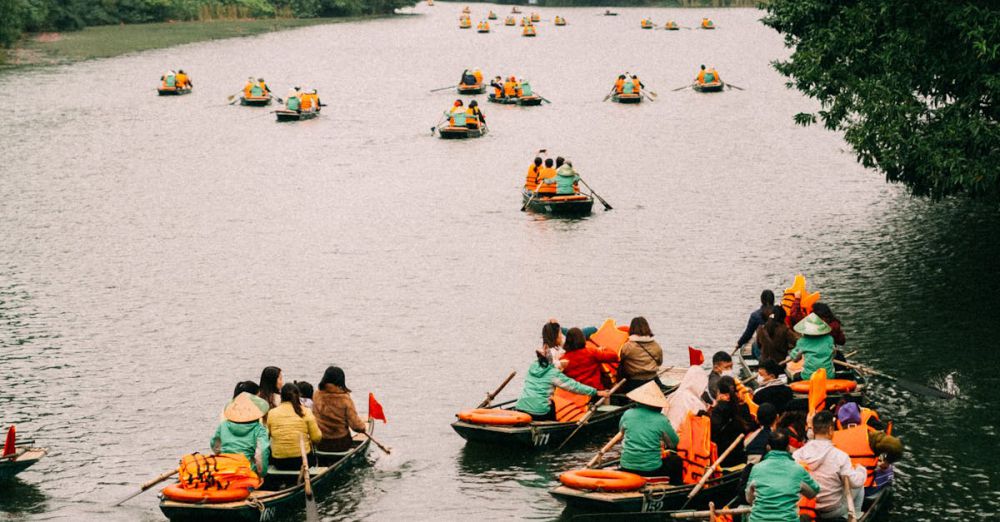 Canoeing Routes - Tourists enjoy a serene rowboat ride on a lush river surrounded by mountains.