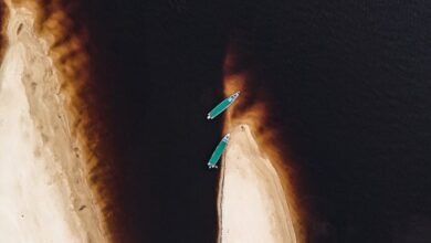 Sea Kayaking - Aerial photo of two kayaks near a dramatic coastal sand formation.