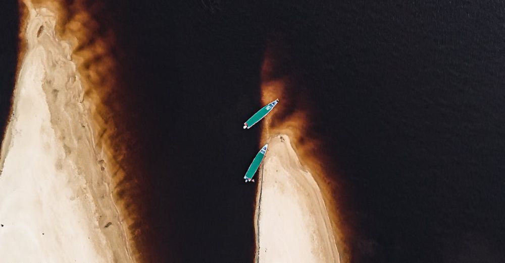 Sea Kayaking - Aerial photo of two kayaks near a dramatic coastal sand formation.