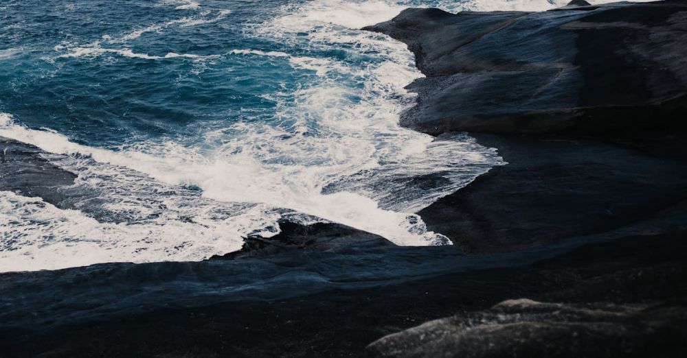 Rough Water - View of ocean waves crashing against a dark rocky shoreline, creating a dramatic seascape.