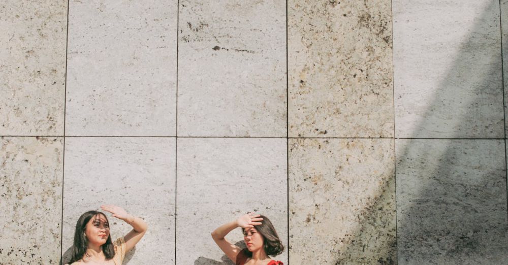 Sun Protection - Two women standing against a stone tile wall shielding eyes from the sun.