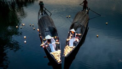 Night Paddling - Drone view of anonymous elegant female putting candle lanterns on river water from boats against male partners in evening