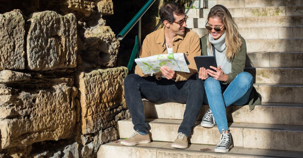 Couple Routes - Smiling couple explores city sitting on stairs with map and tablet.