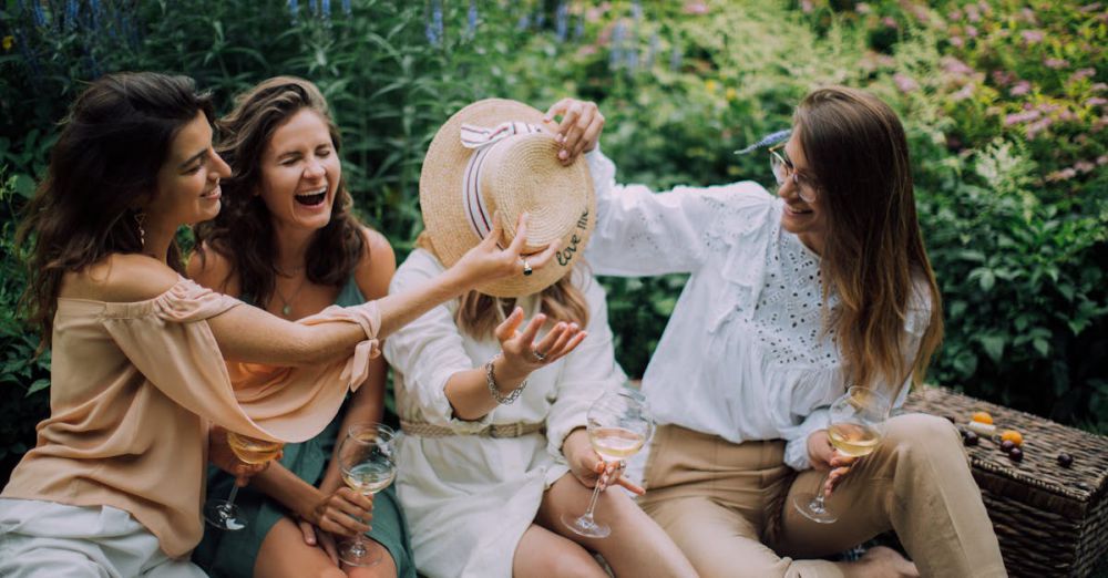 Group Adventures - Four women enjoying a fun, relaxing picnic, sharing wine in a lush garden setting.