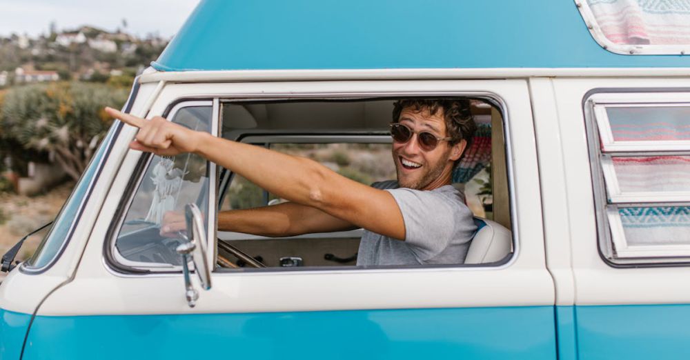 Scenic Routes - Happy man pointing excitedly from inside a vintage blue van on a sunny day.