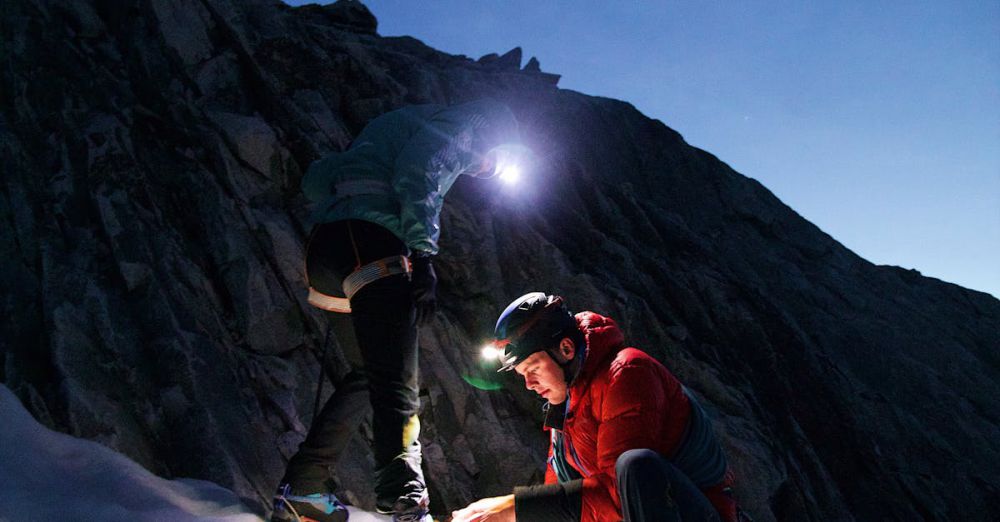 Snowshoeing Safety - Two climbers explore a snowy mountain at dusk, lighting their path.