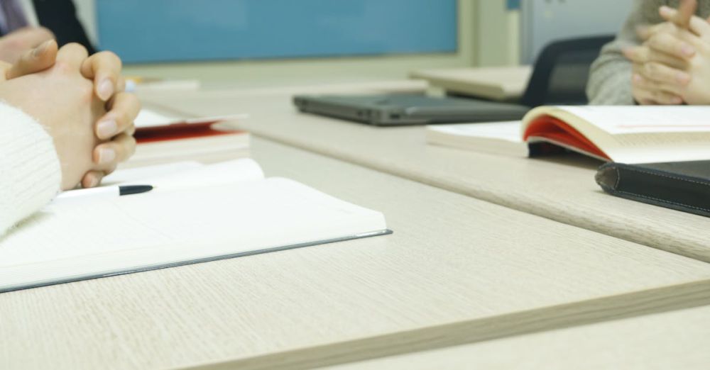 Preparation - Close-up of a professional meeting setup with hands, laptops, and notebooks on a wooden desk.