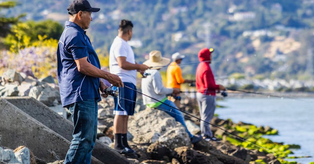 Adventure Tips - Men fishing on a rocky shoreline, enjoying a summer day by the sea.