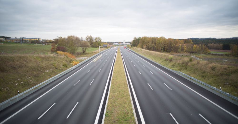 Peaceful Routes - A serene image of an empty highway stretching through a peaceful countryside under a cloudy sky.