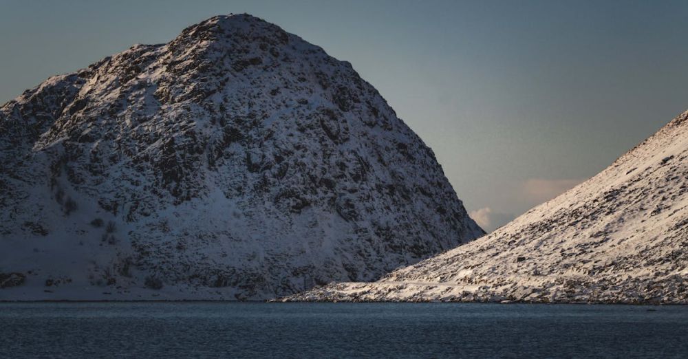 Winter Ice Climbing - Serene snow-covered mountain peaks reflecting in a calm lake under a clear sky.