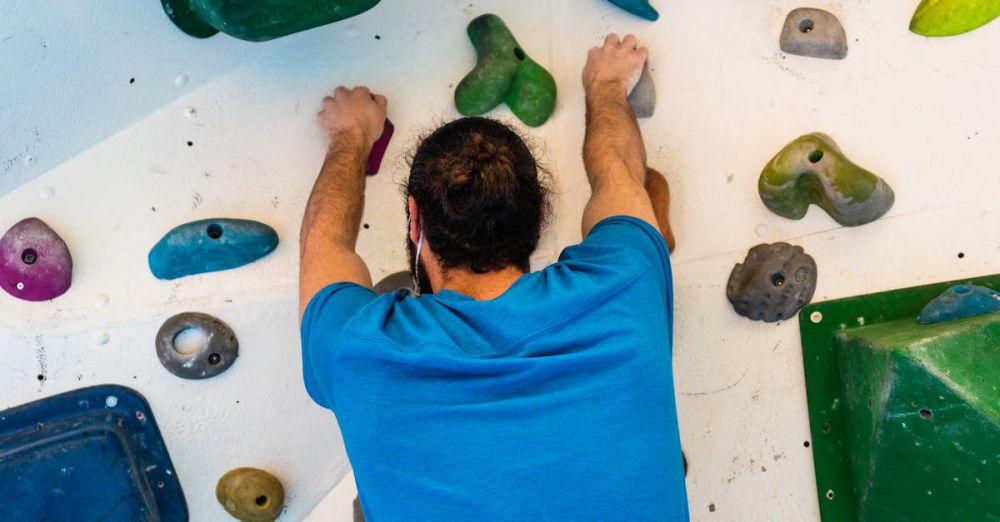 Climbing Experience - Adult male engaged in indoor bouldering, wearing harness with colored holds.