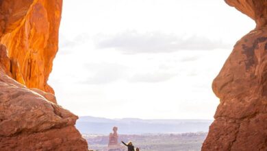 National Park Climbing - Hikers explore a sunlit natural arch in the stunning Arches National Park.