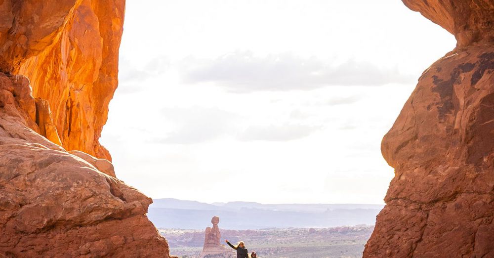 National Park Climbing - Hikers explore a sunlit natural arch in the stunning Arches National Park.