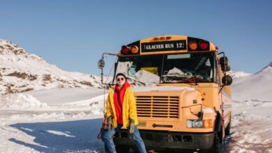 Glacier Tours - Woman in vibrant winter clothing posing next to a glacier tour bus in Icelandic snow landscape during daytime.