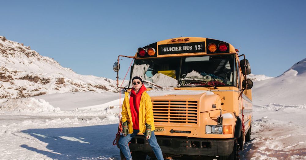 Glacier Tours - Woman in vibrant winter clothing posing next to a glacier tour bus in Icelandic snow landscape during daytime.