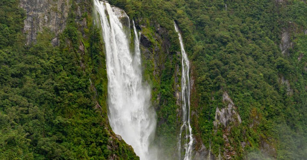 Adventure Tours - Tour boat approaches stunning waterfall in a mist-covered fjord, capturing nature's grandeur and serene beauty.