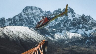 Helicopter Glacier Tours - A vibrant helicopter flies over a tranquil lake framed by majestic Himalayan peaks in Nepal.