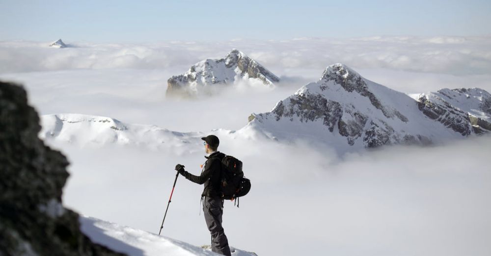 Winter Glacier Tours - A climber stands confidently overlooking a snowy mountain landscape with clouds.