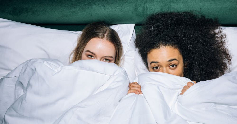 Best Time - Two young women having fun and relaxing under white bedding, illustrating friendship and comfort.