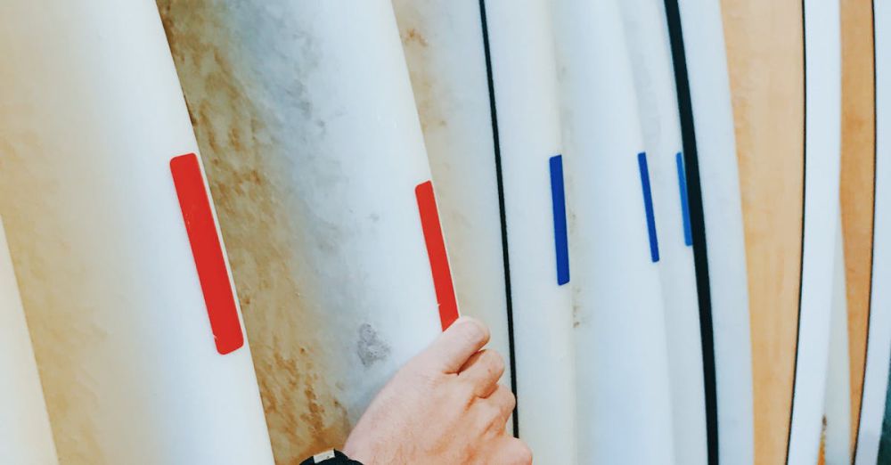 Surfboard Choice - A close-up of a man's hand selecting a surfboard in a shop.