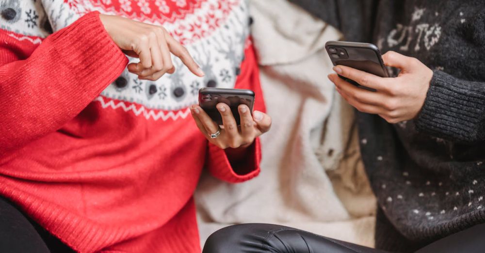 Year-Round Surfing - Two women in festive sweaters using smartphones indoors during winter.