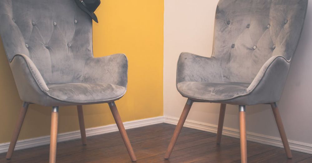 Chairs - Two contemporary gray armchairs in a minimalist interior with a yellow accent wall and wooden flooring.