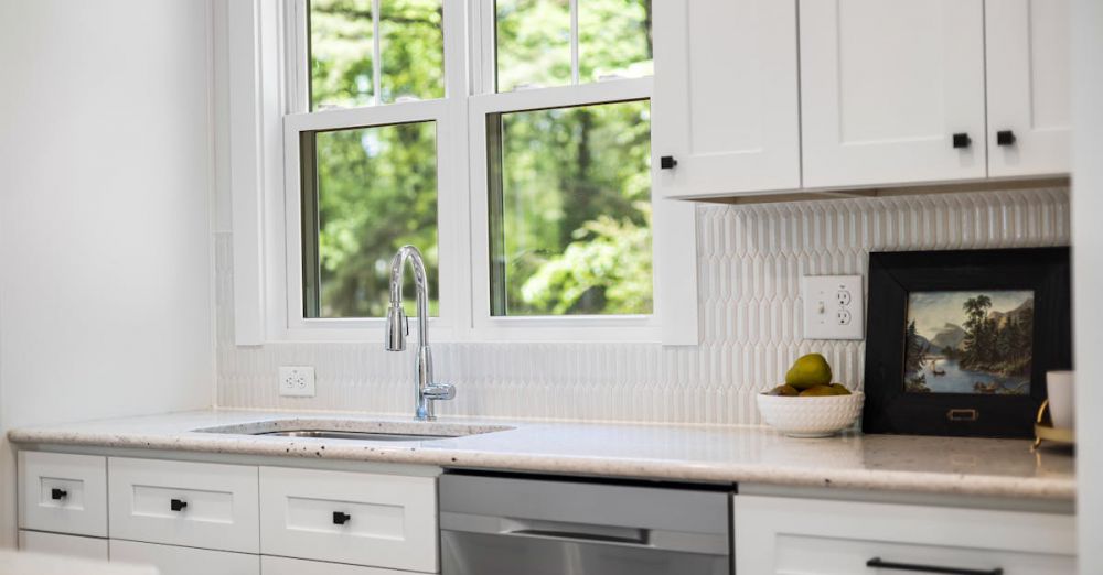 Dishwashers - Contemporary white kitchen interior with natural light, featuring a sink and window view of greenery.