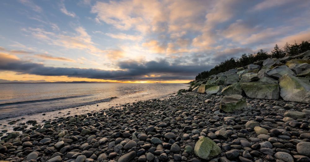 BC Surfing - Beautiful sunset over a rocky beach in Courtenay, BC, with dramatic clouds and calm sea.