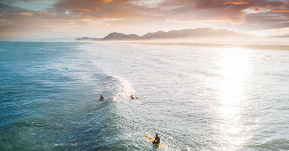 Surfing Trip - Three surfers riding waves under a stunning sunset in Kamchatka, Russia's coastline.