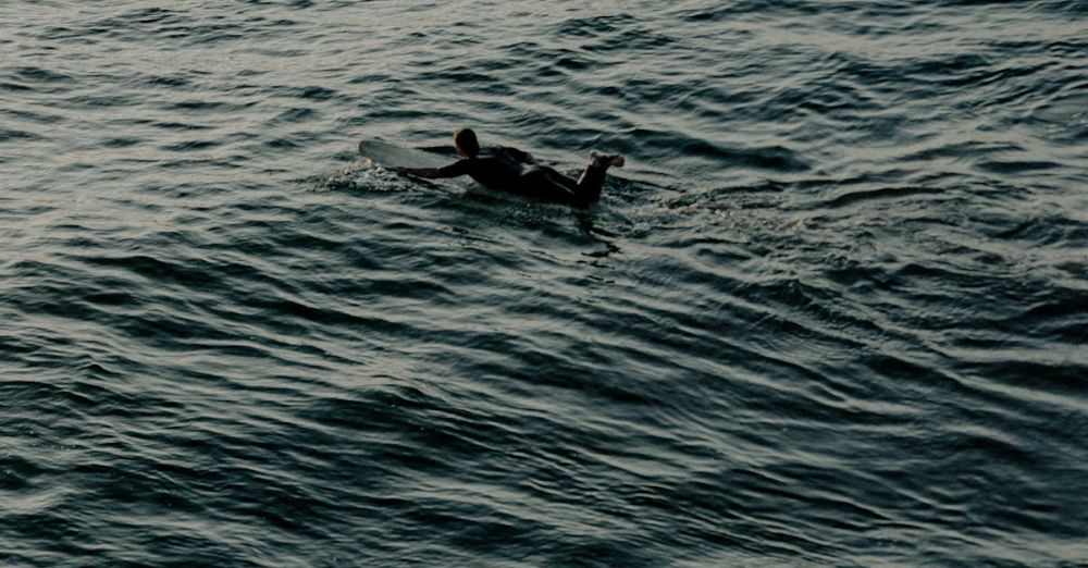 Night Surfing - Surfers in silhouette waiting for waves during twilight, showcasing the calm sea and serene atmosphere.