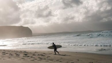 Surfing In Wind - A surfer walks on the beach with a surfboard