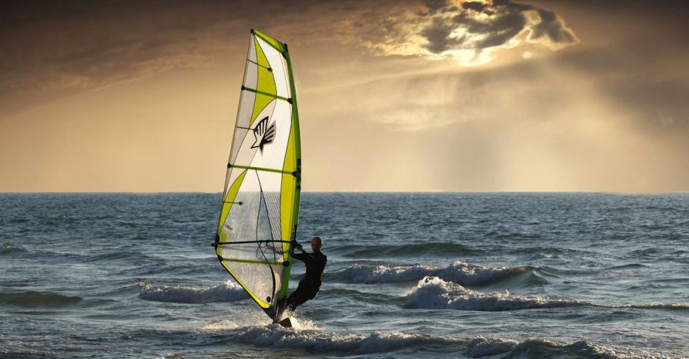 Surfing Vs Windsurfing - Exciting windsurfing action against a dramatic sunset seascape. Perfect for adventure and travel themes.