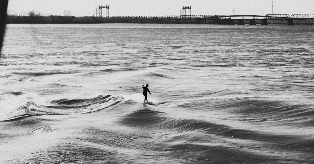 Quebec Surfing - Black and white image of a surfer on a river wave with a bridge in Montreal.