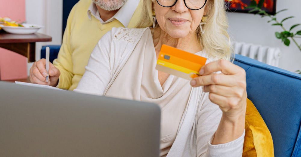 Budget Surfing - Elderly couple smiles as they shop online with a credit card on a cozy couch.