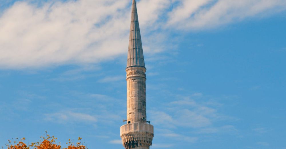 Fall Foliage Destinations - A tall minaret against a blue sky, surrounded by autumn trees in vibrant hues.