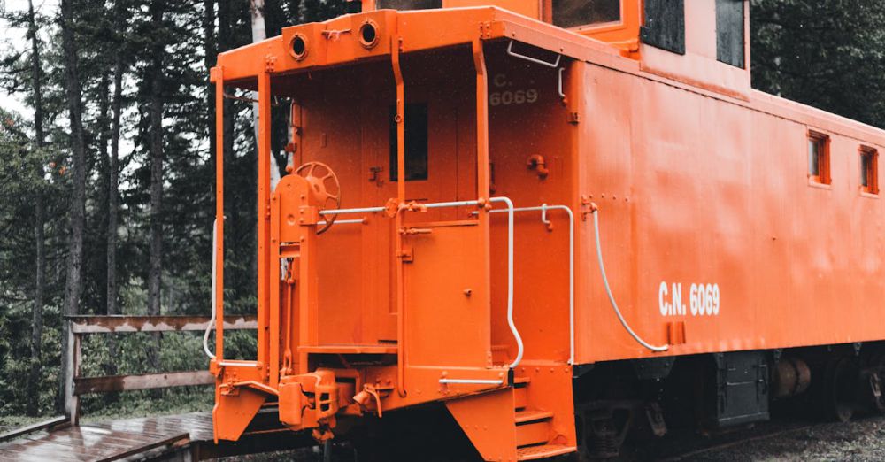 Train Foliage Tours - A bright orange train caboose parked on railway tracks amidst lush forest trees.