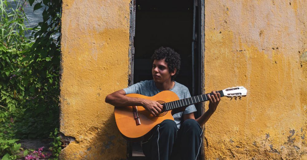 Solo Foliage - A man playing guitar outside a rustic yellow house in Brazil on a sunny day.