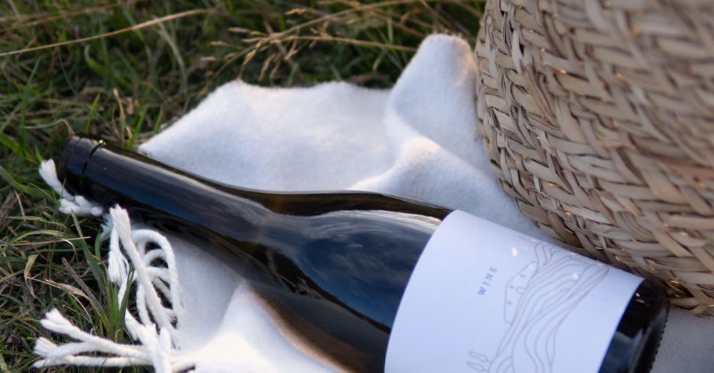 Weekend Getaways - Serene outdoor scene with wicker basket, wine bottle, and blanket on grassy field.