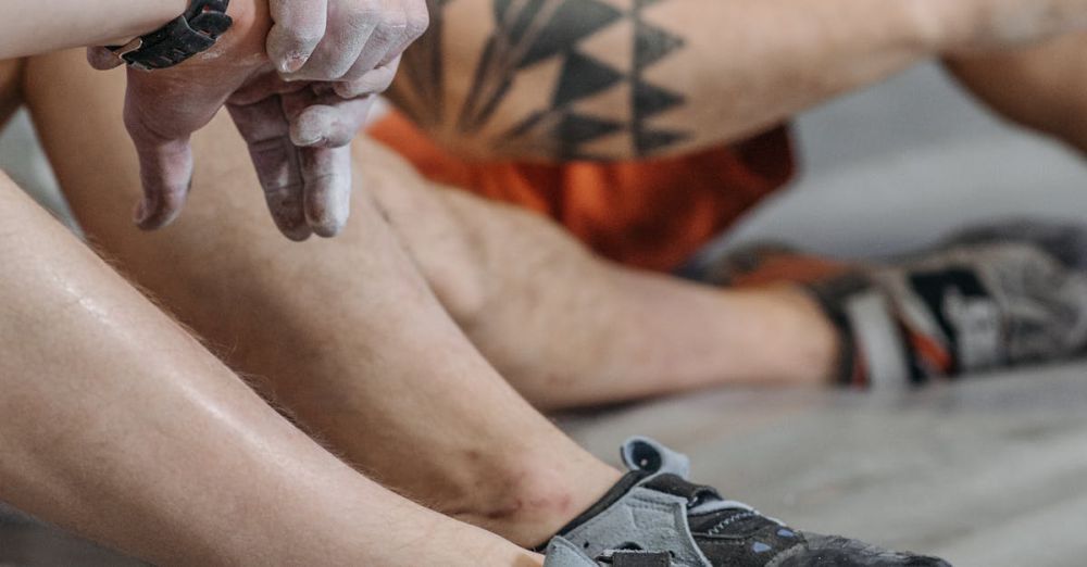 Challenging Climbs - Close-up of tattooed climbers resting with climbing shoes at indoor gym.