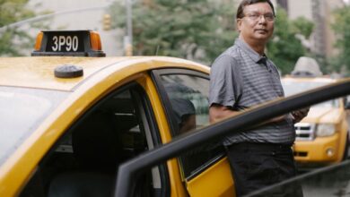 Experiences - Asian taxi driver standing beside a yellow cab in the city with an open door.