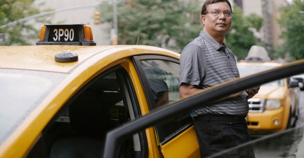 Experiences - Asian taxi driver standing beside a yellow cab in the city with an open door.